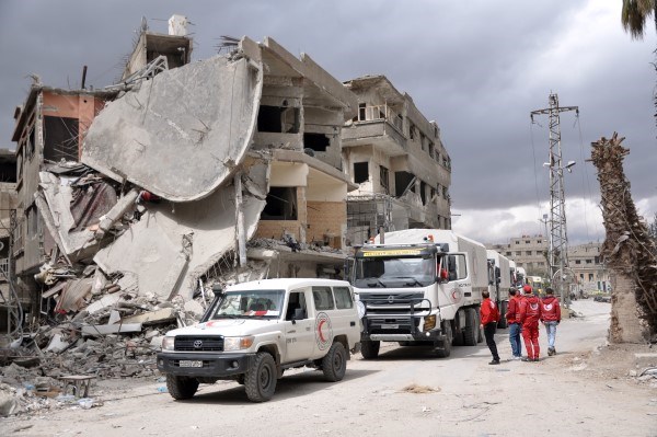 Flere frivillige og lastebiler står foran sønderbombede bygninger