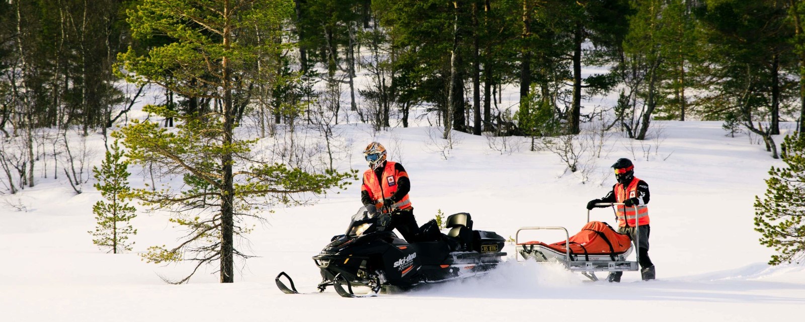 To menn kjører snøskuter i snø. Har hjelpekorpsuniformer.