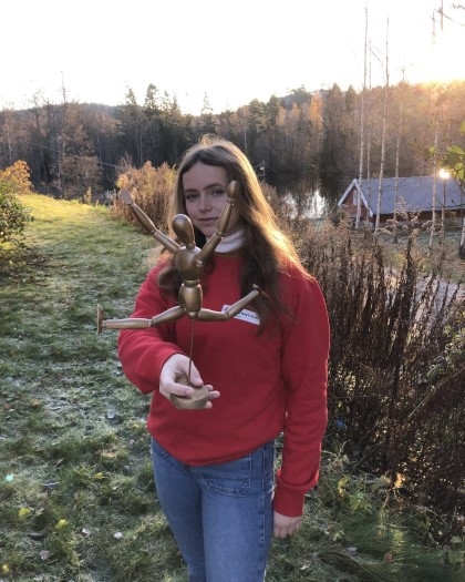 Jente i en hage som holder bevegar menneske figur laget av tre.