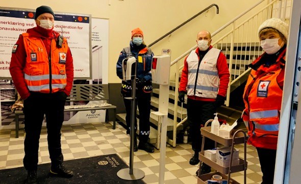 Fire personer med Røde Kors- klær og munnbind står innenfor en inngangsdør.