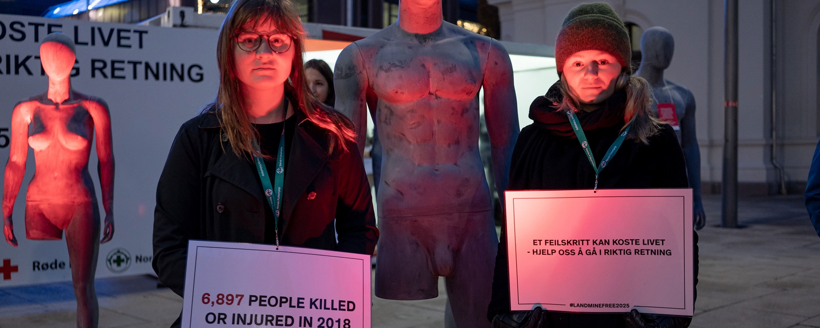 To jenter står med to manekengdukker uten ben og holder skilt med teksten "Et feilskrift koster livet" i forbindelse med tilsynskonferansen for minekonvensjonen i 2019