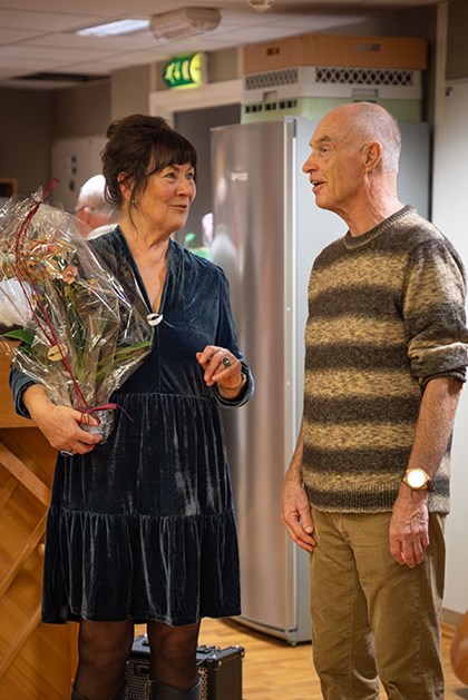 Ei kvinne med blomar i handa står og smiler og prater til ein mann.