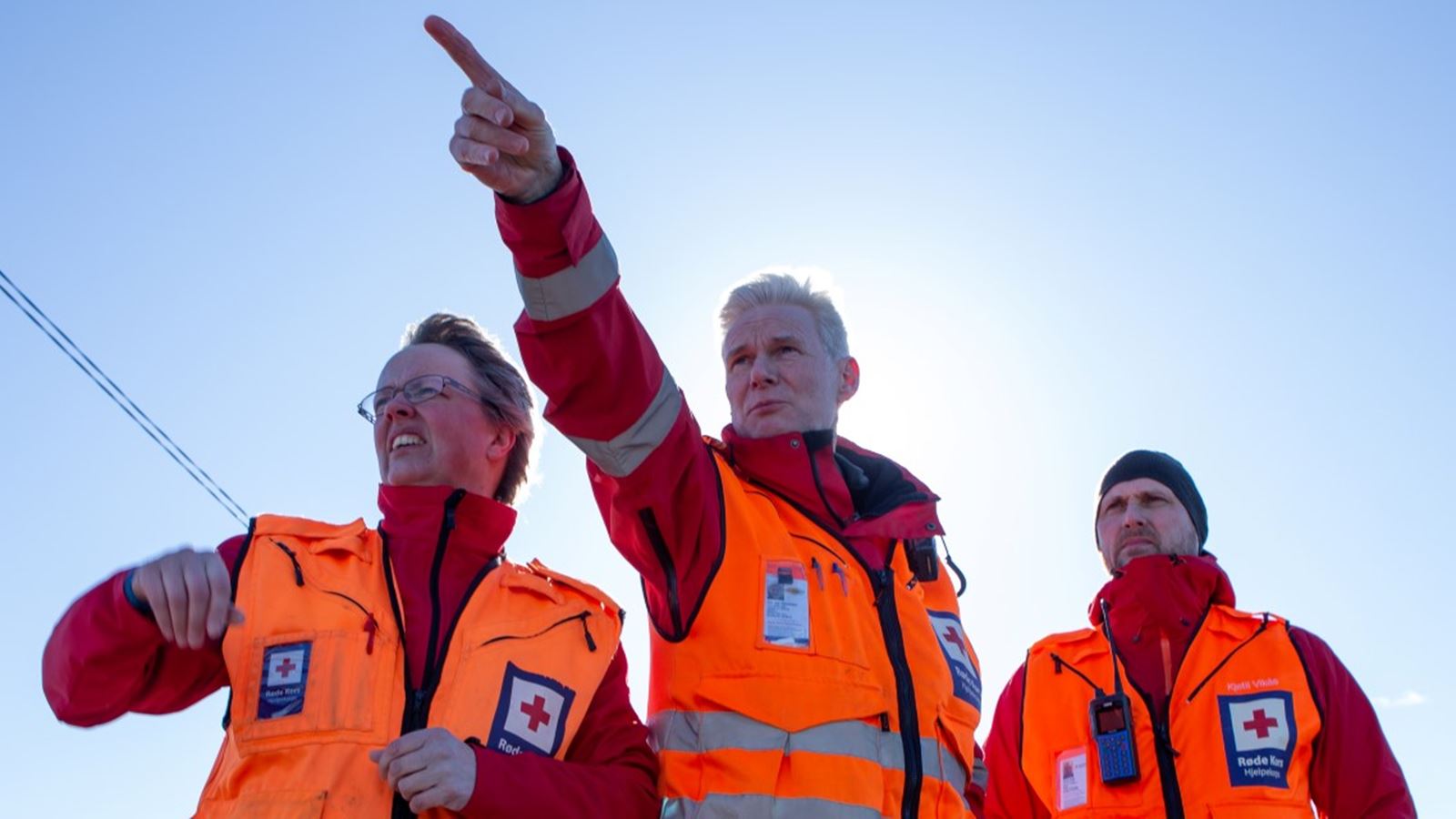 Tre hjelpekorpsere peker ut mot havet