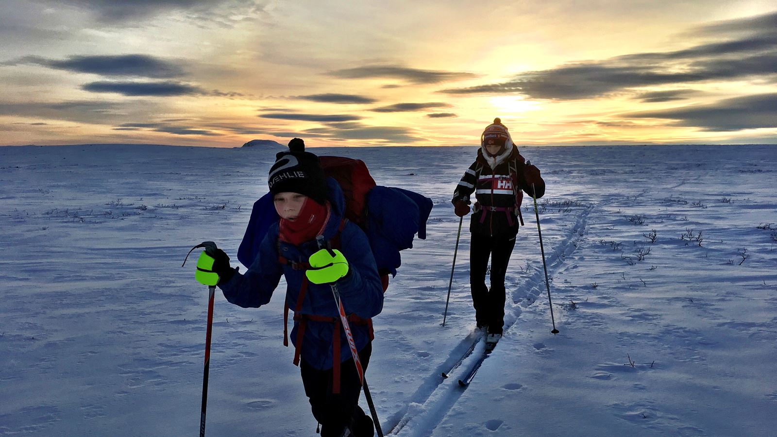 To skiløpere går på vidda med solnedgangen bak seg