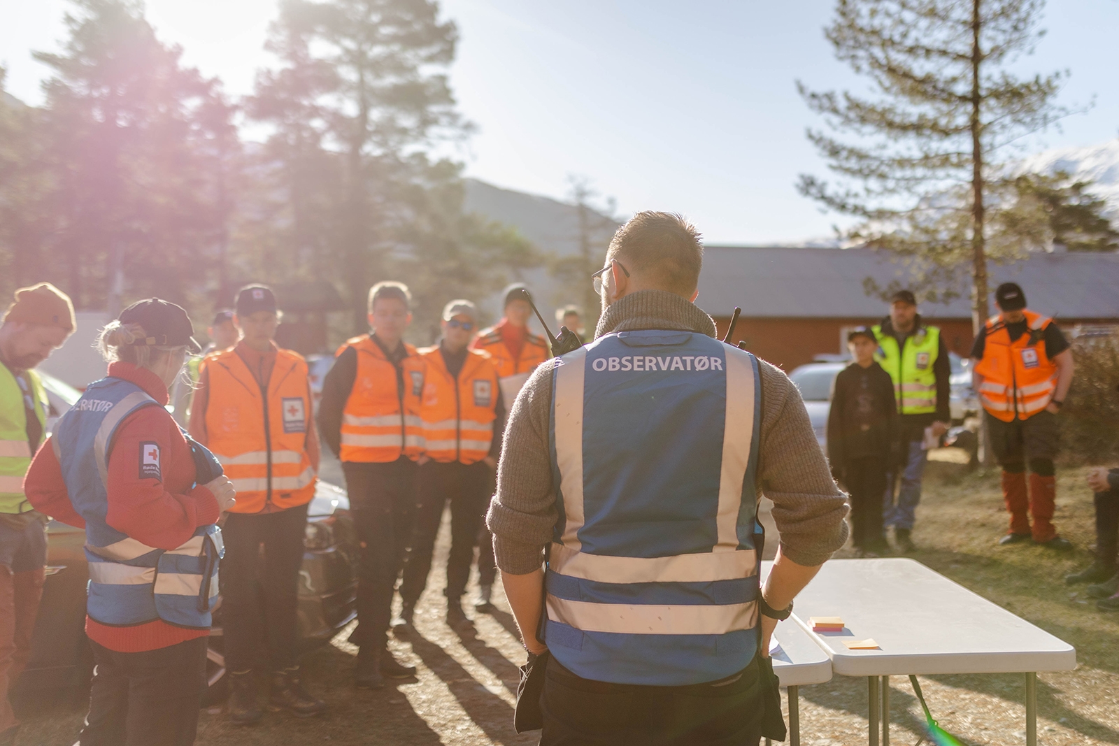 Gruppe med menneske kledd i oransje vest lyttar til instruktør i blå vest