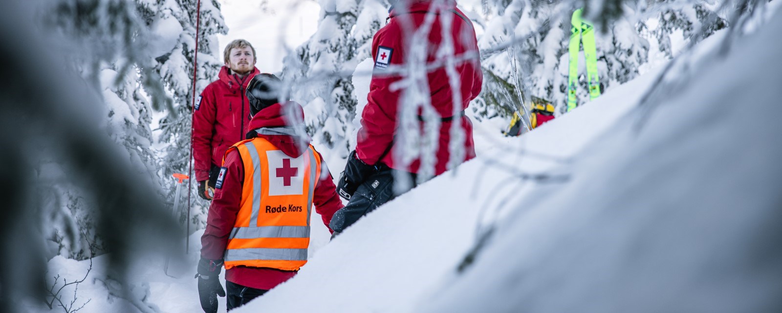 Tre personer med hjelpekorpsuniform står i en snødekket skog