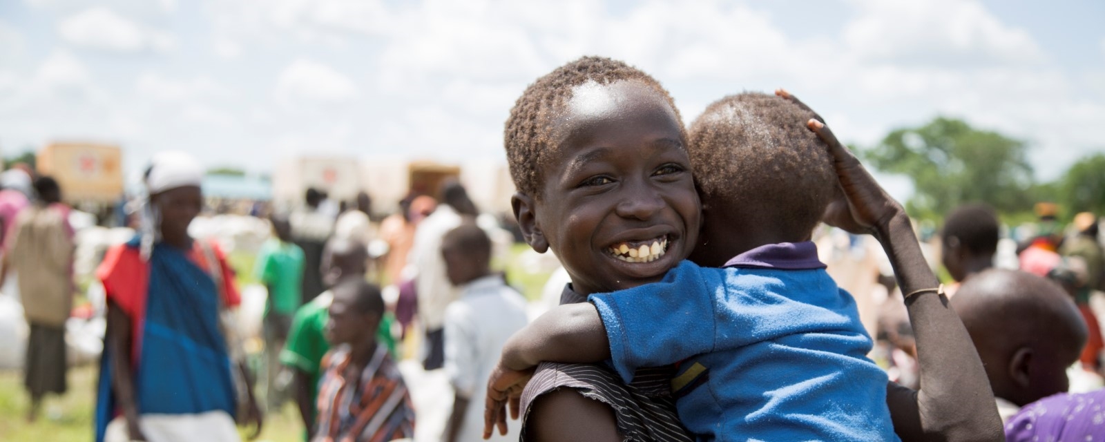 Et barn holder en baby på armen og smiler