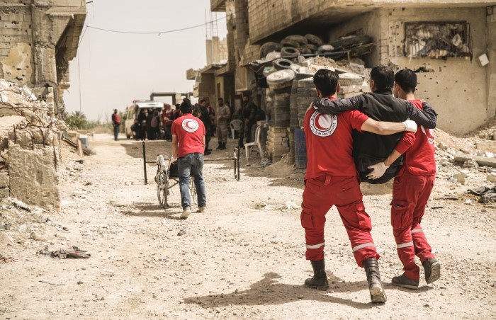 To frivillige bærer en skadet mann gjennom ruiner etter et bombeangrep