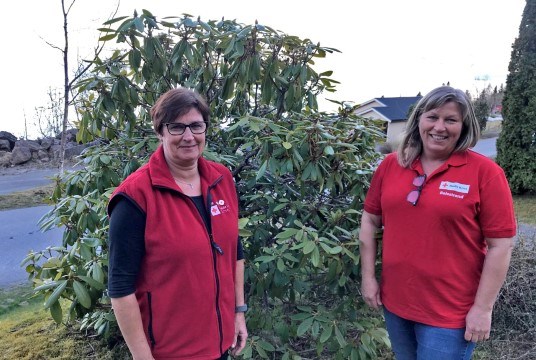 Grete Mo og Anita Hjønnevåg i Balestrand. Dei har på seg Røde Kors-klede og står framfor ein rododendron. 