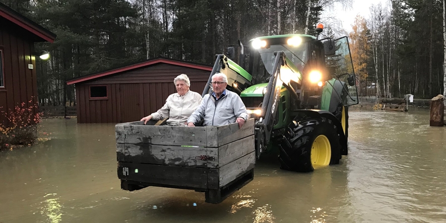 Et eldre ektepar sitter i en kasse på en traktor, og blir fraktet gjennom en flom