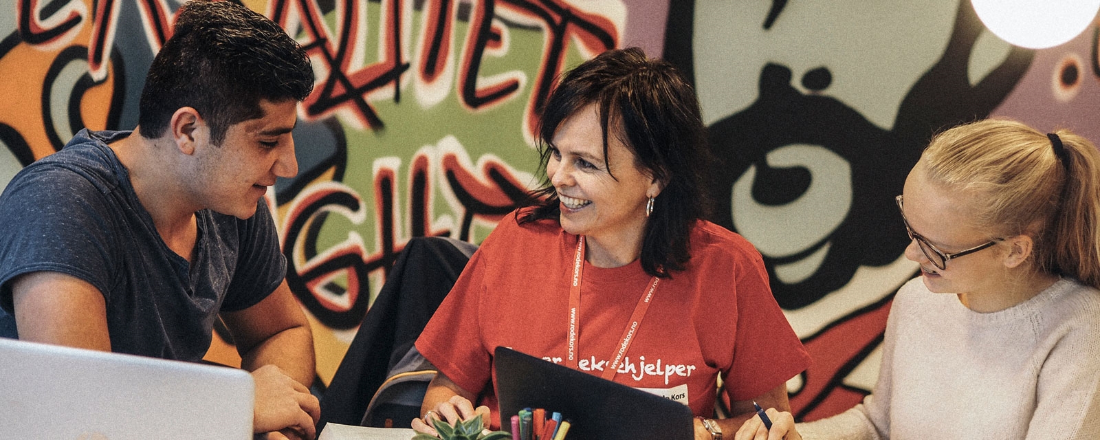 Foto ungdom og en Røde Kors frivillig i munter samtale. Fellesverket et Røde Kors' nasjonale satsing på ungdomsarenaer. Fellesverket er et positivt tiltak som forteller historier om mestring, læring og inspirerende aktiviteter for og med ungdom. 