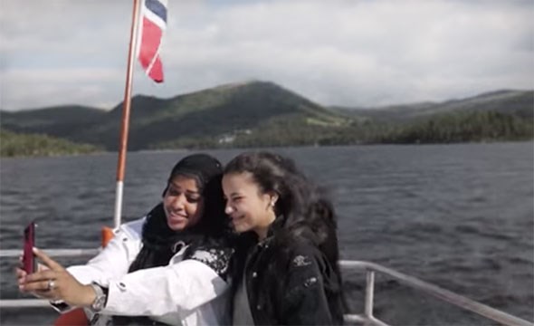 To unge jenter tar selfie i en båt , norsl flagg vaier i baugen 