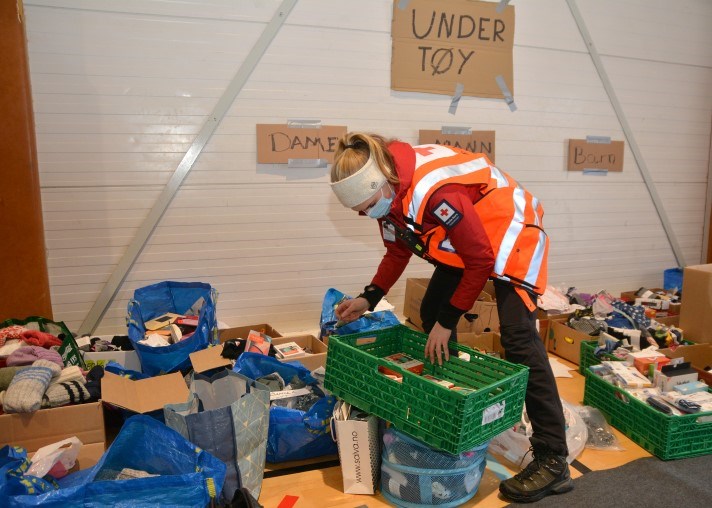 En kvinne i Røde Kors-uniform sorterer klær og utstyr som har blitt samlet inn.