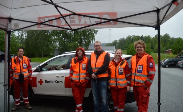 I regnvær står fem i hjelpekorpset under et telt med bilen fra hjelpekorpset bak.