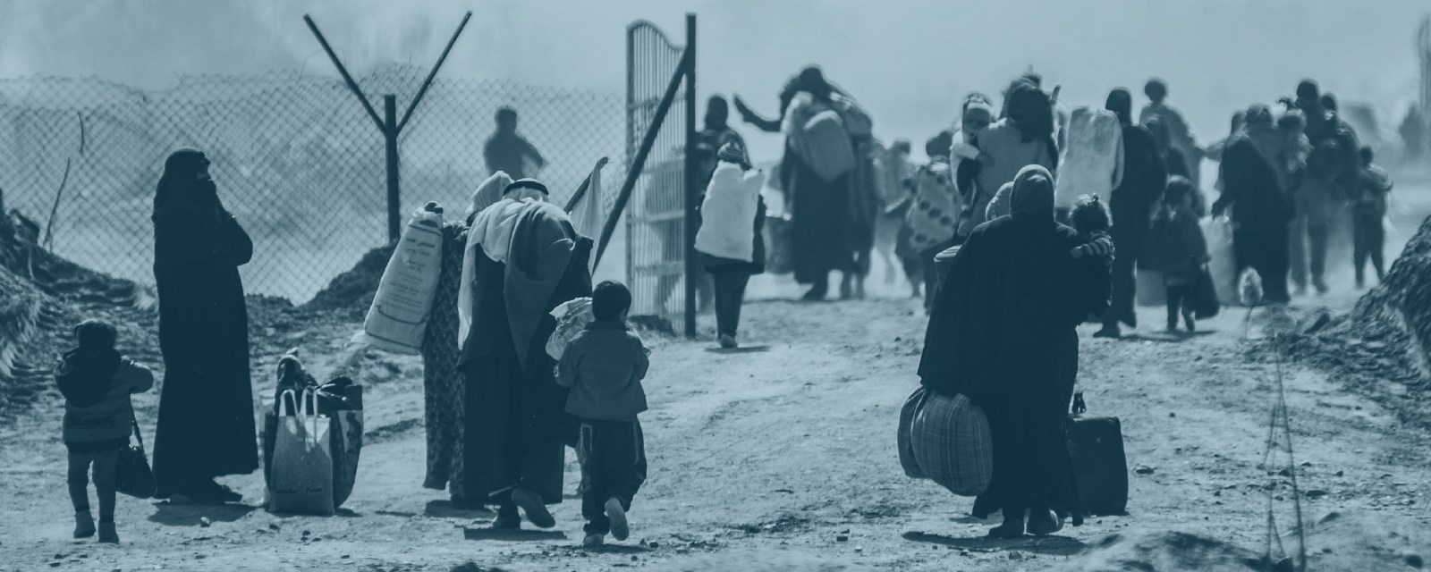 Mange kvinner og barn går langs en støvete vei mot en port