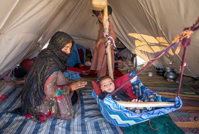 En kvinne sitter i et telt med et lite barn som ligger i en  slags hengekøye