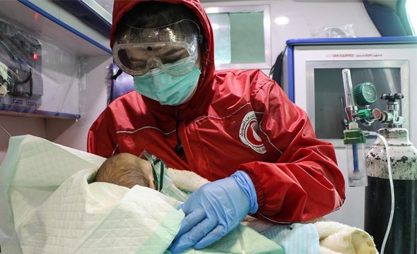 Frivillig i rød jakke og munnbind i ambulanse med liten baby