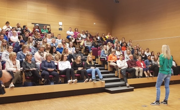 En sal der foredragsholder står foran og presenterer, mens publikum følger med. Setene er fulle av av ungdommer og noen voksne.