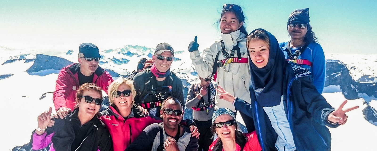 Bildet viser flere personer som smiler på toppen av Galdhøpiggen, Norges høyeste fjell. De er både frivillige og deltakere fra Røde Kors og Turistforeningen. Frivillighet og friluftsliv er to aktiviteter som kan bidra til bedre mental sunnhet.