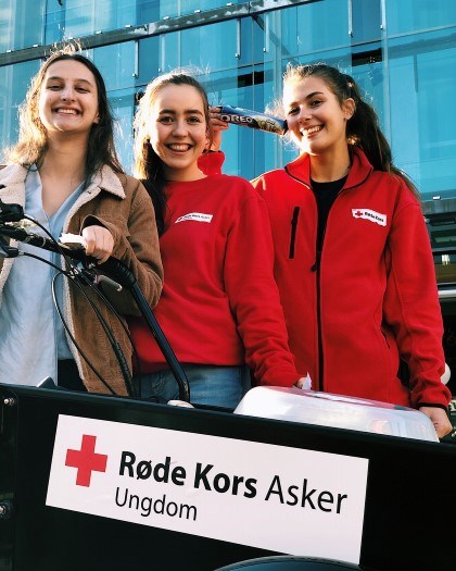 Tre jenter som står foran et skilt som sier at de er ungdom i Røde Kors Asker