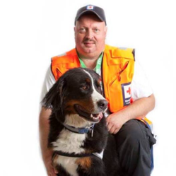 Mannlig hjelpekorpser med hund sitter og smiler til kamera.