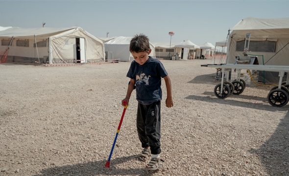 Liten gutt på krykke foran hvite telt