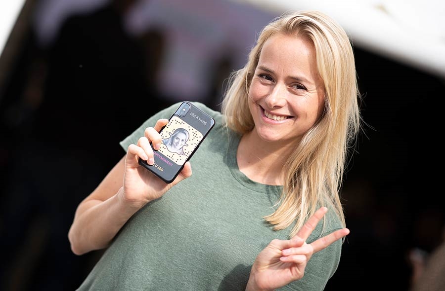 Blond kvinne smiler og gjør V tegn, holder mobil med snapchat ikon