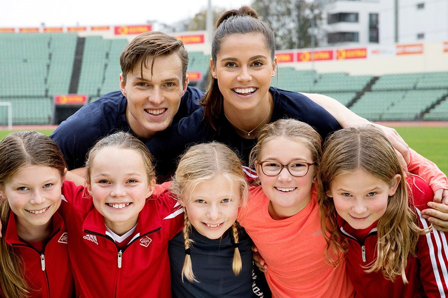 Bilde av 2 voksne og fem unge jenter smiler ser og siler mot kamera, ute, stadion