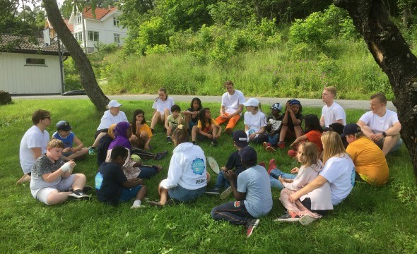 Deltakere og instruktører på camp Solvik sitter i en sirkel på gresset.