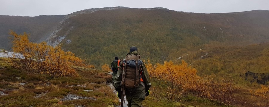 I et øsende regnvær går en gruppe mennesker på rekke i et oransje fjellandskap om høsten. 