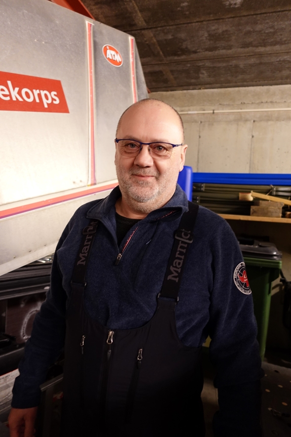 Mann i garasje med tilhenger i bakgrunnen.