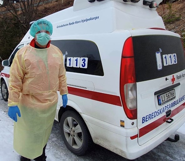 Person med smittevernutstyr foran en ambulanse