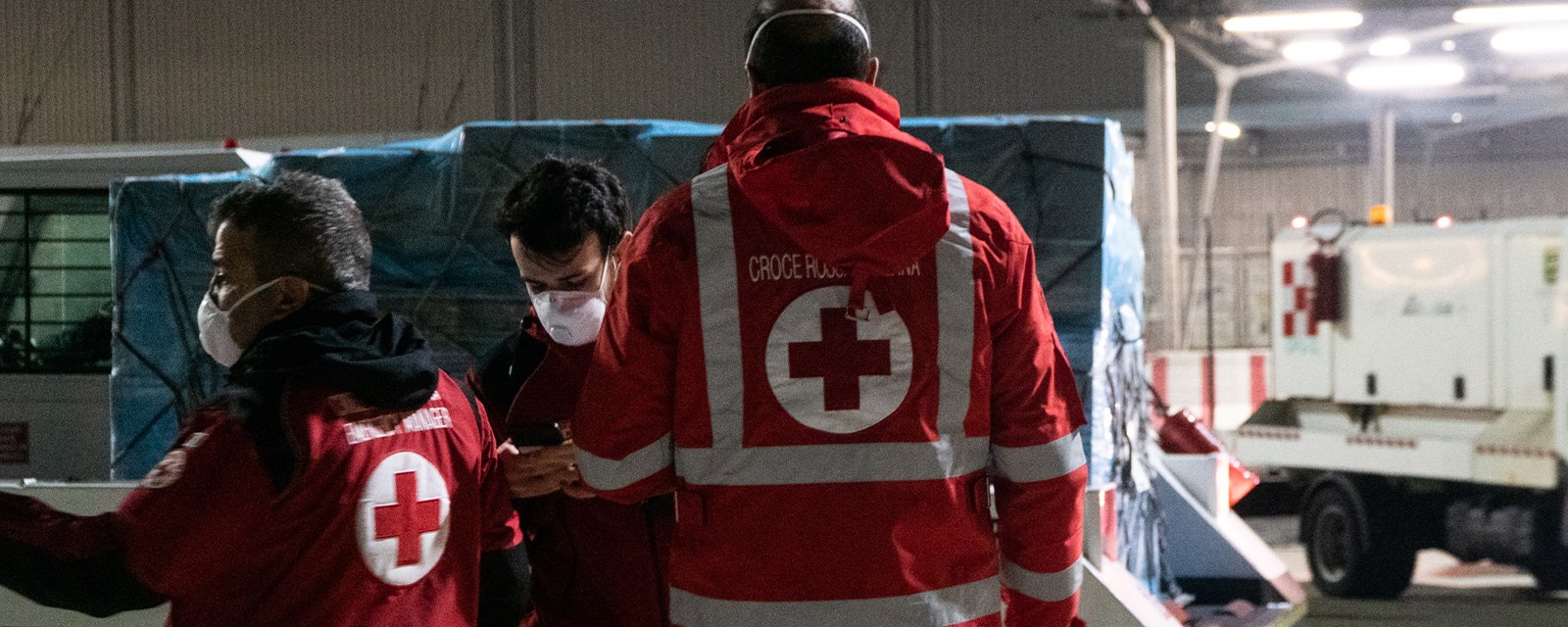 Tre menn med Røde Kors-jakke og munnbind