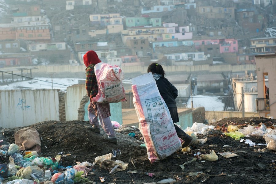 To barn går med svære poser på en søppelfylling