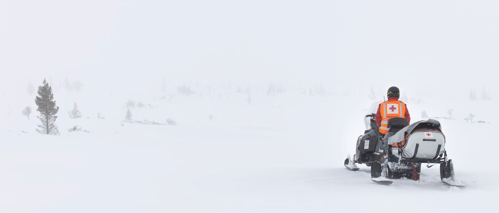 Røde Kors mannskap i snøvær som sitter på en snøscooter
