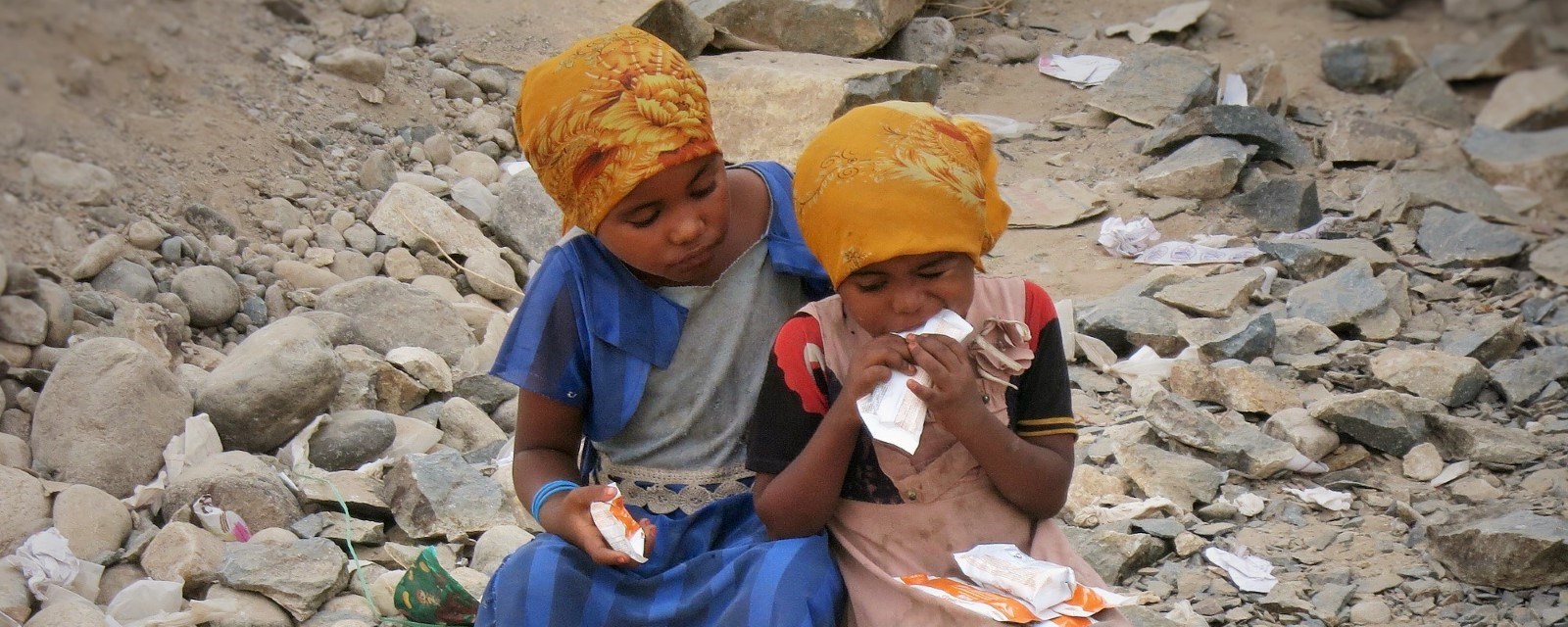 To barn sitter i en steinrøys og spiser matrasjoner. 