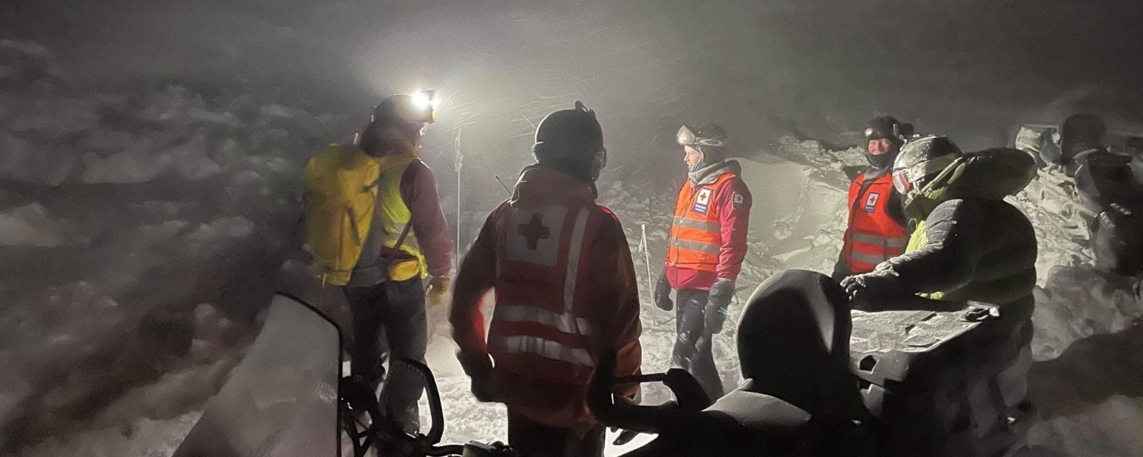 A volunteer from the Norwegian red cross sits on a snow scooter in a mountain landscape in wintertime. 