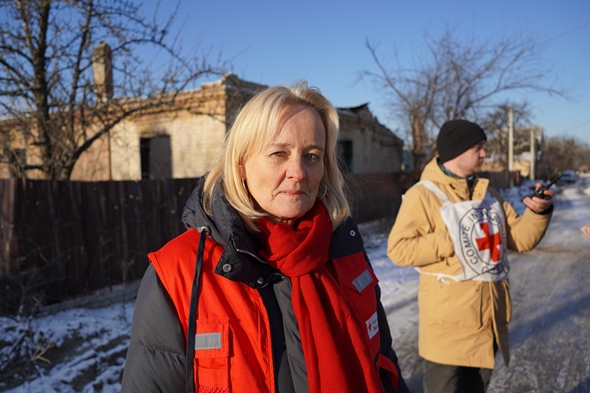 Kvinne utendørs, i en gate rammet av krigshandlinger, ser i kamera