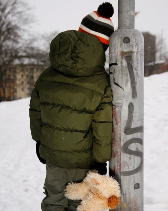 Et barn står med ryggen til med en bamse i hånda.