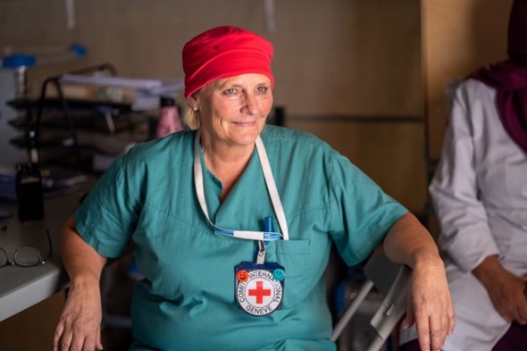 En kvinne i grønt sykepleierunifor med Røde Kors emblem på brystet sitter i et telt