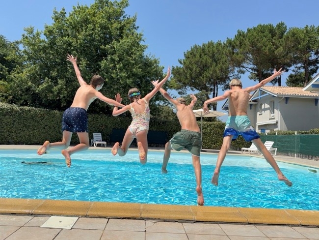 4 barn hopper ut i et svømmebasseng for å kjøle seg ned i sommervarmen.