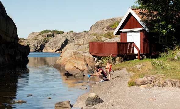 En far og et barn sitter ved strandkanten og leker.