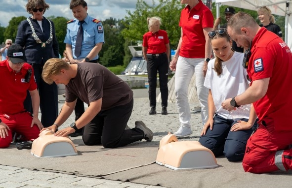 To personer øver på hjerte- og lungeredning med øvingsdukner med to instruktører som veileder dem.
