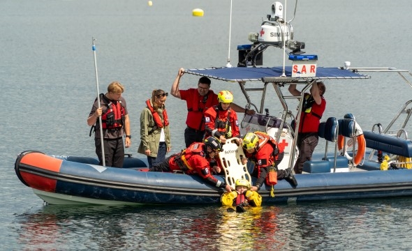 En båt med redningsfolk øver på vannledning og drar opp en person fra sjøen.
