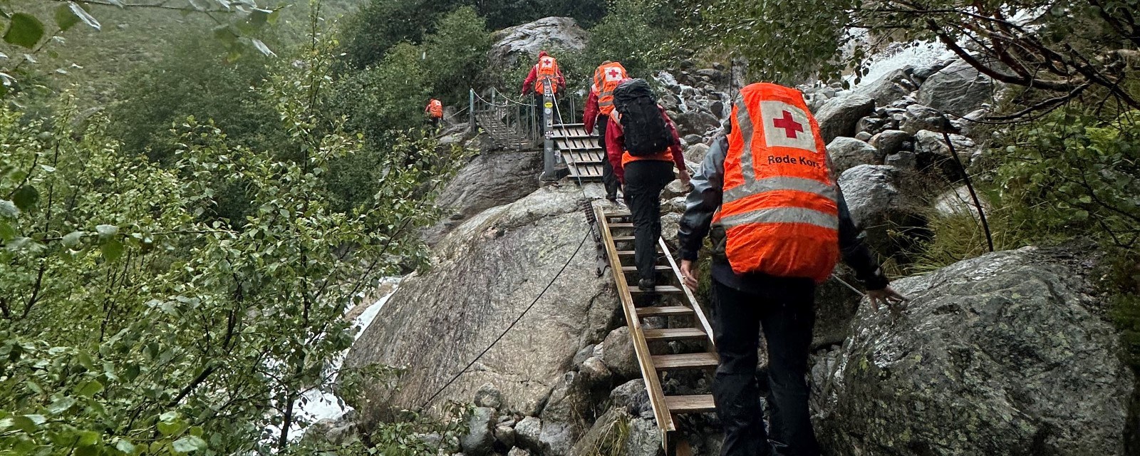 En gruppe frivillige fra Røde Kors klatrer oppover en trapp i bratt fjellterreng for å lete etter en savnet person.