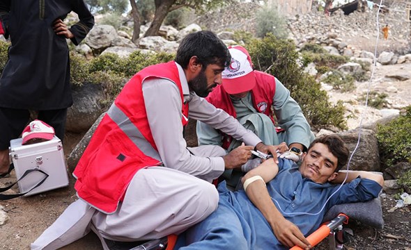 En frivillig fra Røde Halvmåne gir førstehjelp til en mann som ligger på bakken.