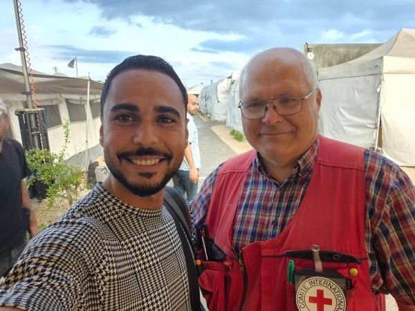 To menn smiler. De står utenfor noen oppsatte telt på et feltsykehus i Gaza.