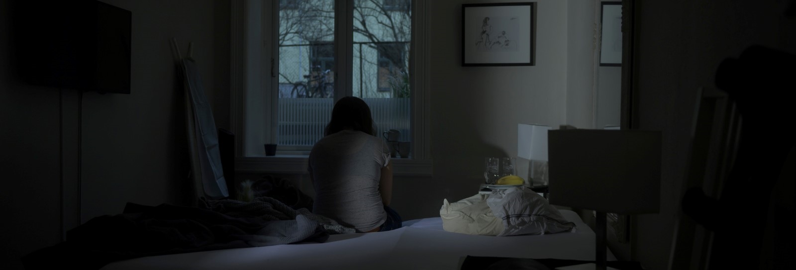 Person sitter i mørket på en seng