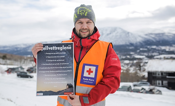 Frivillig fra hjelpekorpset viser frem plakat med fjellvettreglene