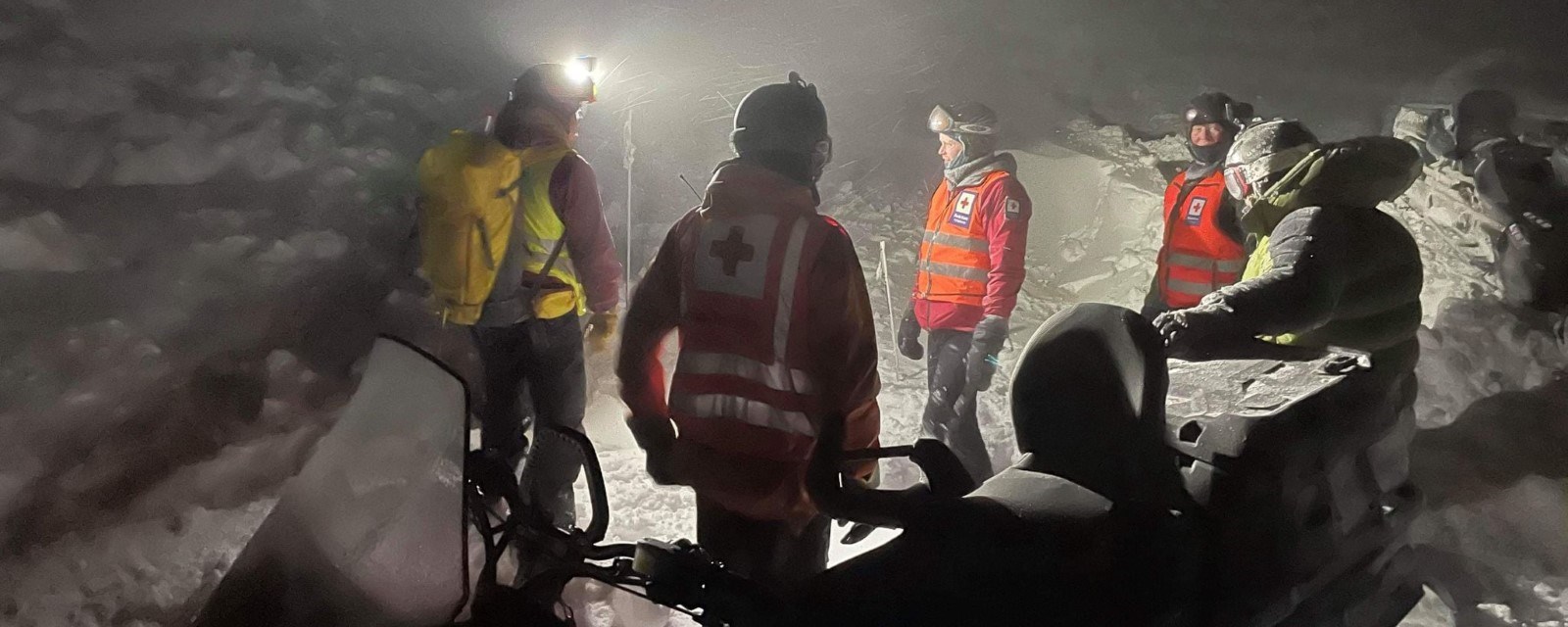 Mannskap på fem fra Røde Kors Hjelpekorps står ute i snøstorm ved tre snøscootere.